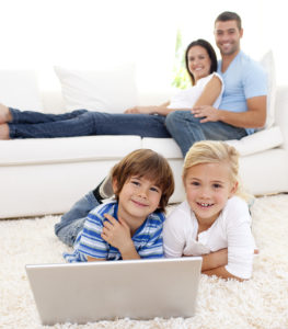 Children playing with a laptop and parents lying on sofa
